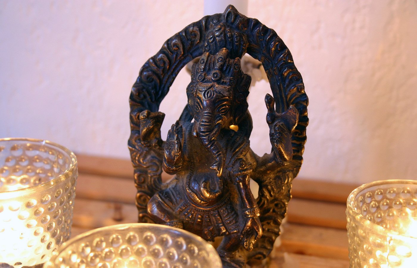 Statuette de Ganesh en bronze sous une arche sculptée, entourée de bougies dans des photophores de verre.