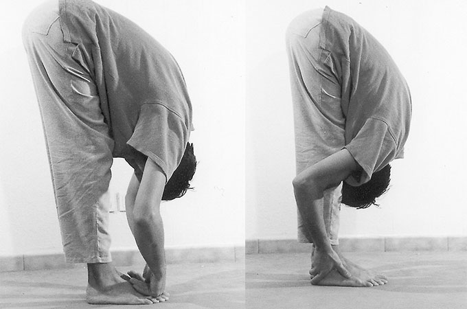Pâdahastâsana en deux temps : debout, le buste replié vers l’avant, les mains glissées sous la plante des pieds.