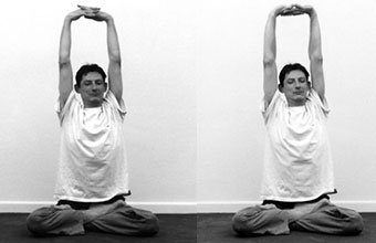 Parvatāsana : assise en tailleur, les bras tendus au-dessus de la tête, les doigts croisés et les paumes tournées vers le ciel.